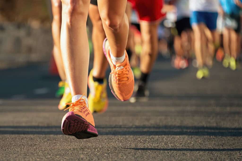 Close-up of runners' shoes and legs mid-race on a road while in motion.