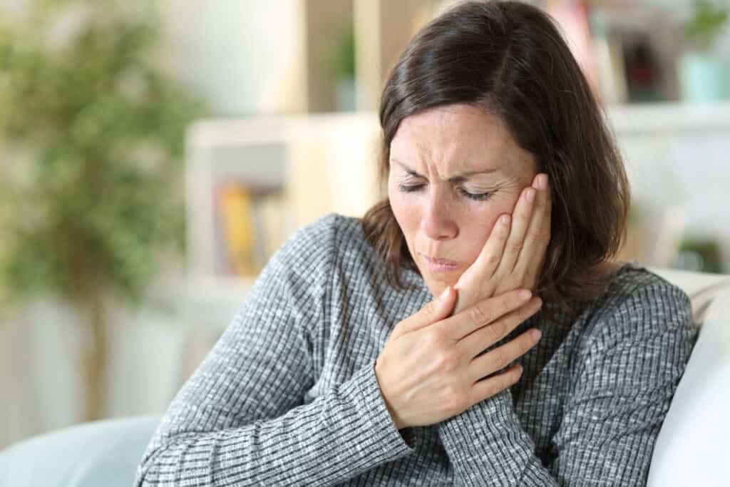Woman holding her hand to her jaw wincing in pain.