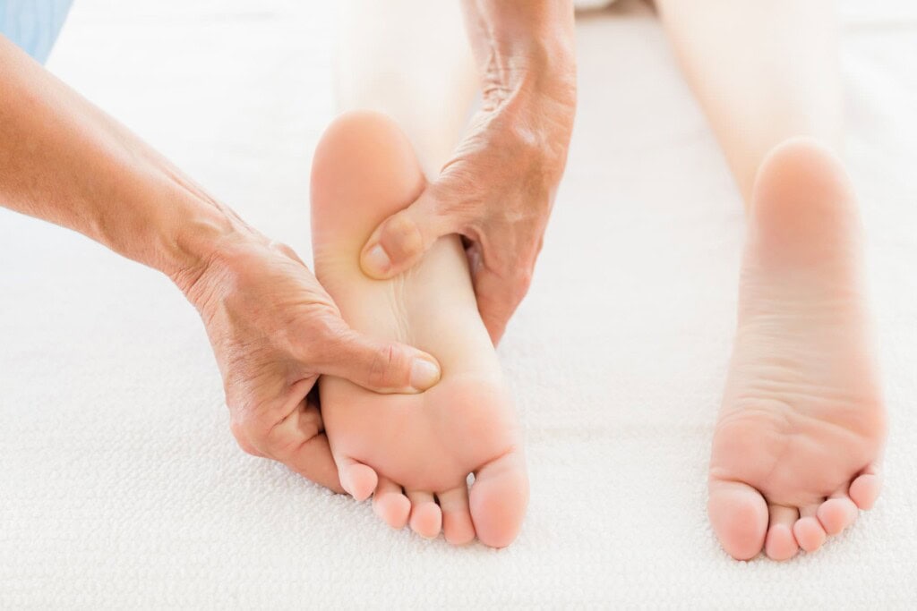 A person receiving a foot massage while lying on a white surface, with another person using their hands to apply pressure to the sole.