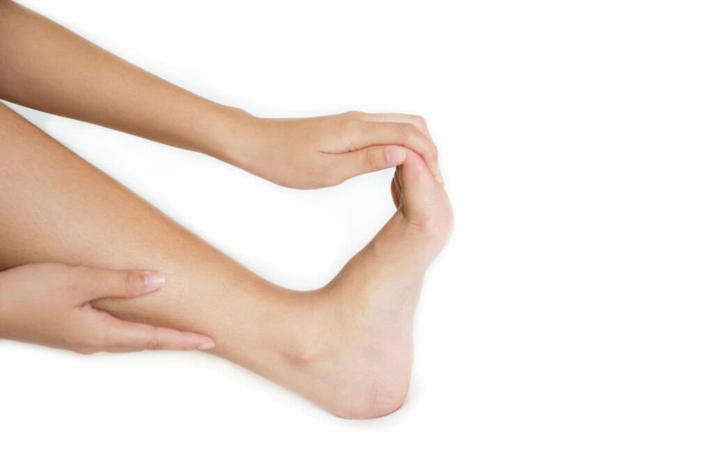 A person performs a foot stretch, extending their right foot and toes with their hands against a white background.