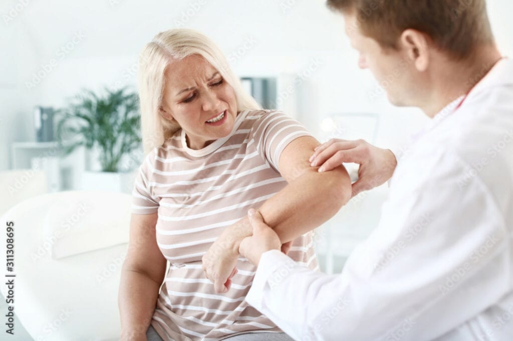 Medical professional examining mature woman with elbow joint pain in clinic.