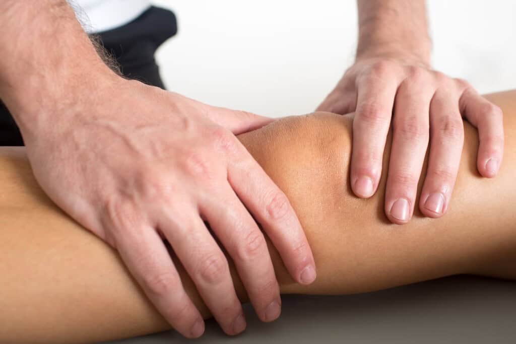 Close-up of hands performing bodywork on a person's knee, addressing issues like IT band syndrome.