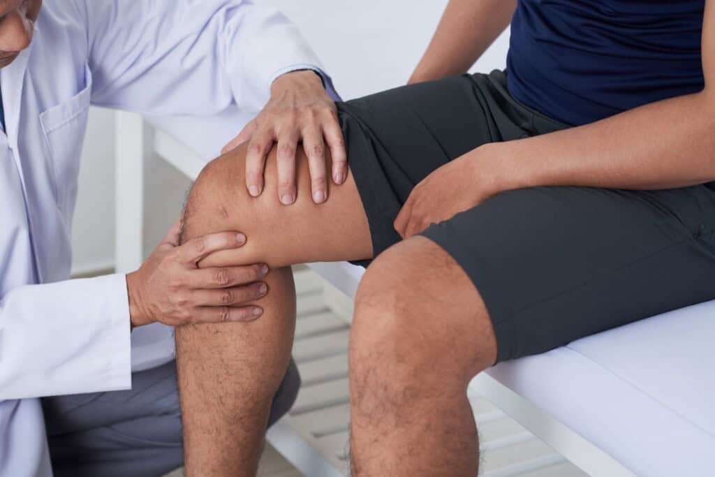 Medical professional examining a male's knee to determine the cause of his pain.