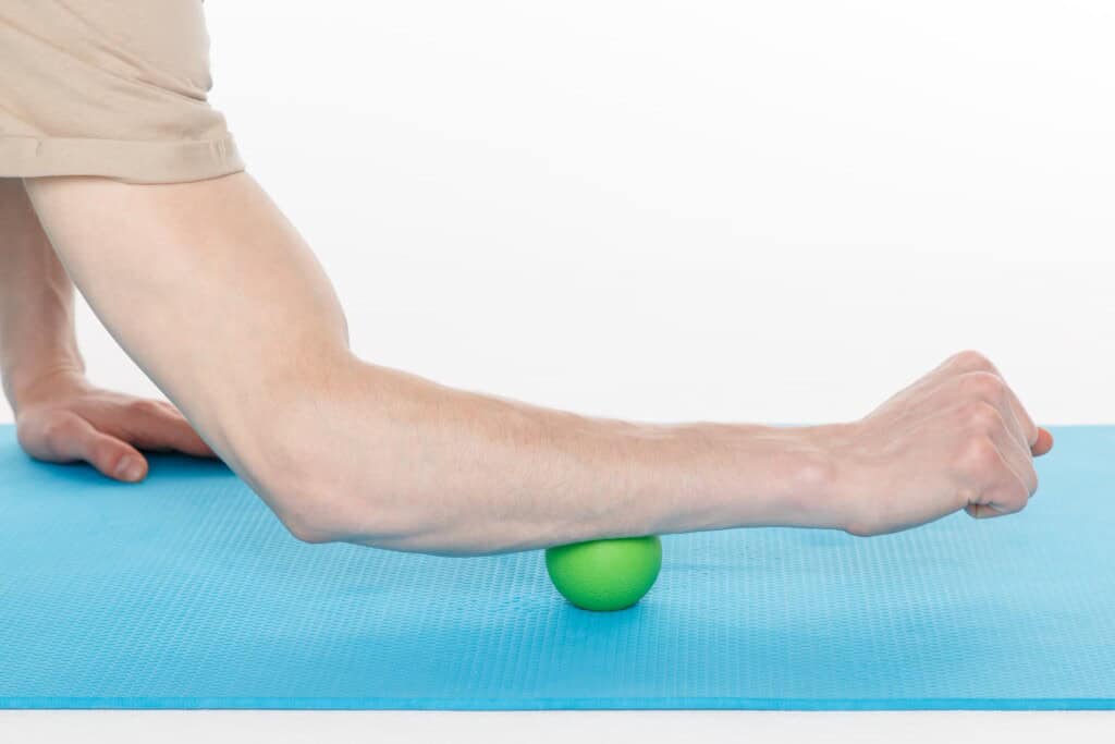 A man's arm performing myofascial release by rolling a massage ball under his forearm to relieve tennis elbow pain.