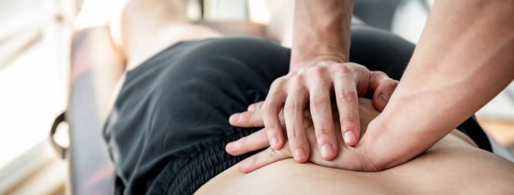 Close-up of a person receiving a back massage, with the bodyworker's hands pressing on the client's upper back to alleviate tension and hip pain.