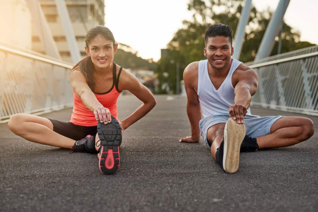 A woman and a man sitting on the bridge stretching their calf muscles before working out.