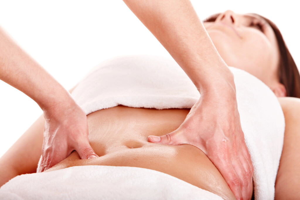 A close-up of a woman receiving an abdominal massage from a bodyworker as part of a treatment for c-section pain. She is comfortably covered with a white towel.