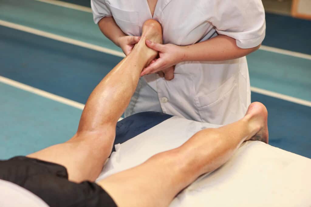 A bodyworker in a white coat performs myofascial release on an client lying on a massage table, focusing on alleviating Achilles tendon pain.