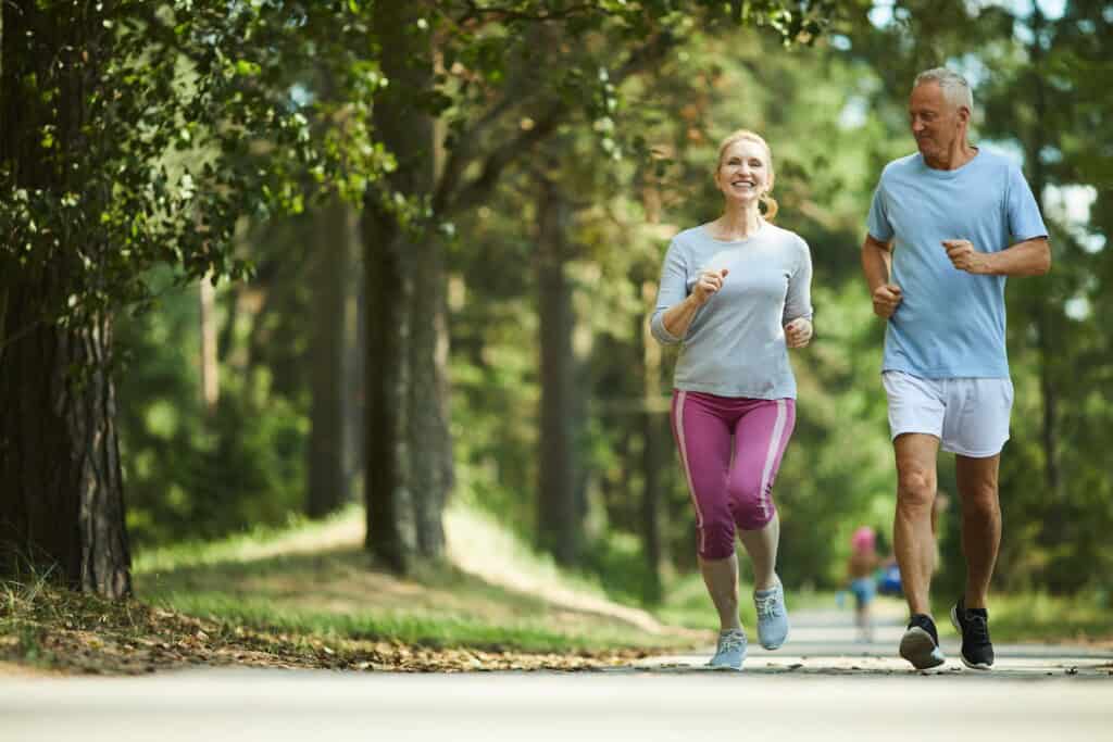 Healthy active senior couple in sportswear running among green trees on a beautiful sunny day.