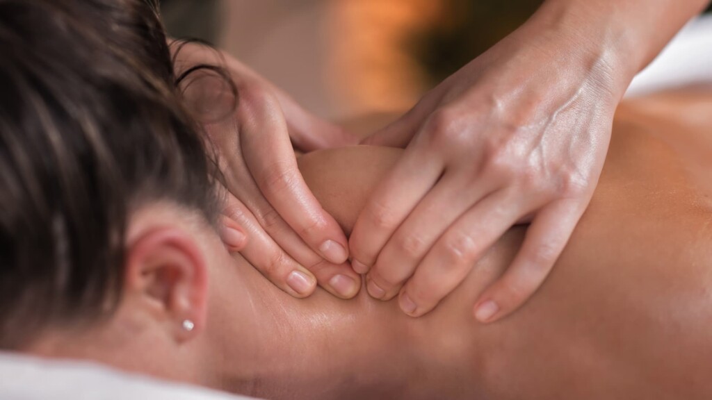 Close-up of hands performing skilled bodywork on a person's neck to relieve whiplash, with the person lying face down on a massage table.