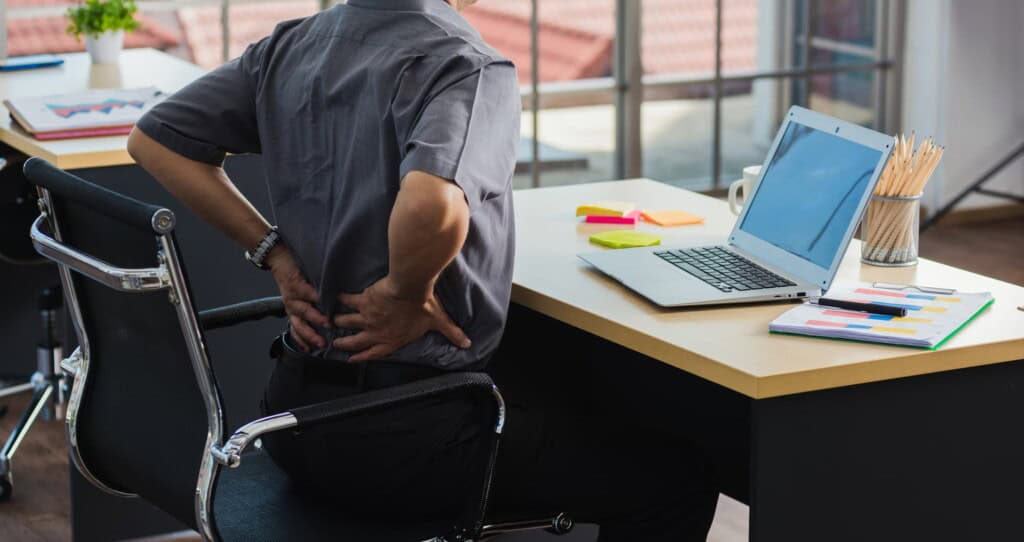 A businessman at his desk gripping his back in pain.