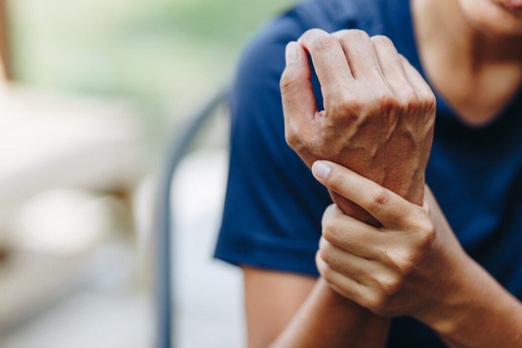 Close-up of a sprained wrist being gently supported by a woman in a blue shirt, in an outdoor setting.