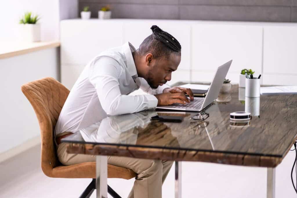 A man is hunched over his desk working on his laptop.