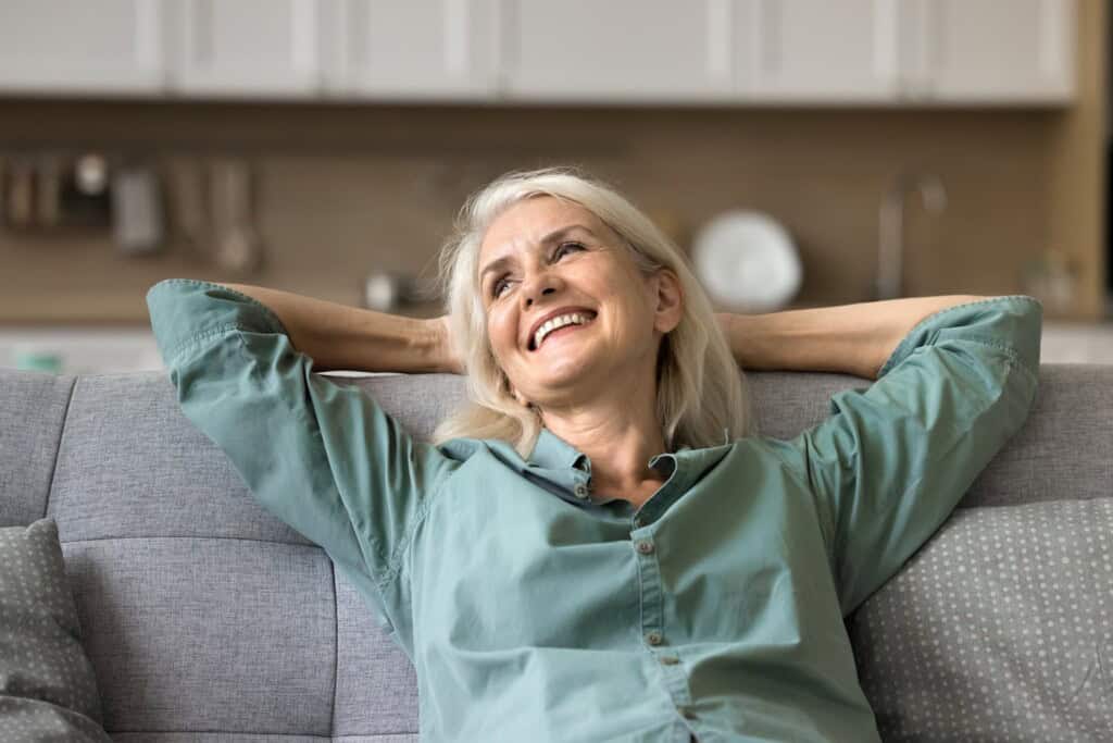 Happy older woman relaxing on a cozy couch, smiling as she enjoys comfort at home.