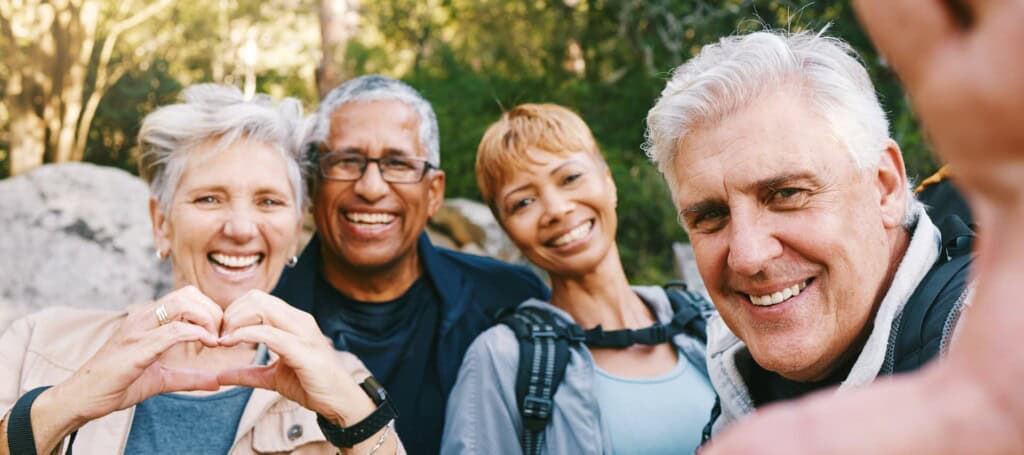 A cheerful group of elderly people smiles while trekking through the woods, promoting wellness, health, and exercise in a scenic outdoor setting.